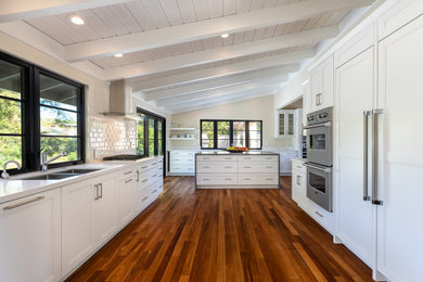 Example of a large trendy galley dark wood floor, brown floor and vaulted ceiling eat-in kitchen design in San Francisco with an island, an undermount sink, shaker cabinets, white cabinets, quartzite countertops, white backsplash, subway tile backsplash, white appliances and white countertops