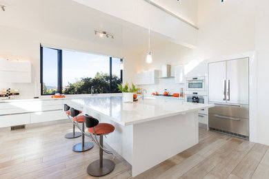 Large minimalist l-shaped light wood floor and beige floor open concept kitchen photo in San Francisco with a drop-in sink, flat-panel cabinets, white cabinets, quartz countertops, white backsplash, white appliances, an island and white countertops