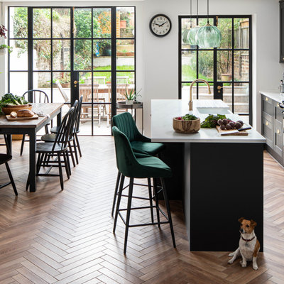 Example of a transitional galley medium tone wood floor and brown floor kitchen design in London with a farmhouse sink, shaker cabinets, black cabinets, an island and white countertops