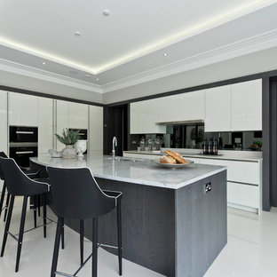This is an example of a contemporary l-shaped kitchen in Surrey with flat-panel cabinets, white cabinets, black splashback, black appliances, an island and white floors.