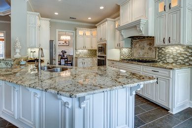 Bild på ett avskilt, mellanstort vintage u-kök, med en dubbel diskho, luckor med upphöjd panel, vita skåp, granitbänkskiva, flerfärgad stänkskydd, stänkskydd i stickkakel, rostfria vitvaror, klinkergolv i porslin, en halv köksö och brunt golv