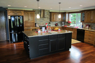 Example of a large classic l-shaped medium tone wood floor eat-in kitchen design in Portland with an island, raised-panel cabinets, dark wood cabinets, granite countertops, beige backsplash, stone tile backsplash, black appliances and an undermount sink