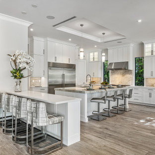 Photo of a contemporary u-shaped eat-in kitchen in Miami with an undermount sink, shaker cabinets, white cabinets, marble benchtops, beige splashback, marble splashback, stainless steel appliances, medium hardwood floors, with island, brown floor, white benchtop and coffered.