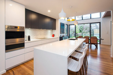 Offene, Mittelgroße Moderne Küche mit Doppelwaschbecken, Quarzwerkstein-Arbeitsplatte, Küchengeräten aus Edelstahl, braunem Holzboden und Kücheninsel in Brisbane