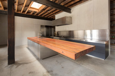 Inredning av ett industriellt stort kök med öppen planlösning, med träbänkskiva, stänkskydd med metallisk yta, betonggolv, en köksö och grått golv