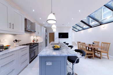 This is an example of a medium sized contemporary single-wall open plan kitchen in Surrey with a submerged sink, shaker cabinets, marble worktops, black appliances, an island and marble flooring.