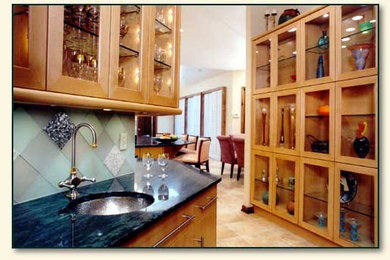 Mid-sized elegant galley linoleum floor eat-in kitchen photo in Jacksonville with an undermount sink, glass-front cabinets, light wood cabinets, soapstone countertops, green backsplash, glass tile backsplash, stainless steel appliances and an island