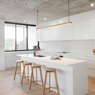 Design ideas for a large contemporary l-shaped kitchen in Sydney with an undermount sink, flat-panel cabinets, white cabinets, white splashback, porcelain splashback, panelled appliances, with island, beige floor and white benchtop.