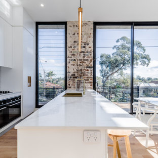 Design ideas for a large contemporary galley eat-in kitchen in Sydney with a double-bowl sink, flat-panel cabinets, white cabinets, white splashback, porcelain splashback, panelled appliances, light hardwood floors, with island, beige floor and white benchtop.