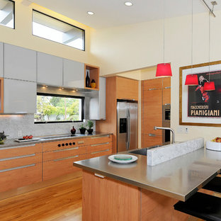 This is an example of a modern kitchen in San Francisco with stainless steel appliances, stainless steel benchtops, an integrated sink, flat-panel cabinets, medium wood cabinets, white splashback and stone slab splashback.