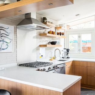 Immagine di una cucina ad U minimalista con lavello sottopiano, ante lisce, ante in legno chiaro, paraspruzzi a effetto metallico, elettrodomestici in acciaio inossidabile e penisola