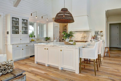 This is an example of a large farmhouse l-shaped kitchen/diner in Charleston with white cabinets, light hardwood flooring, an island, marble worktops, white appliances, a submerged sink, grey splashback, stone slab splashback and shaker cabinets.