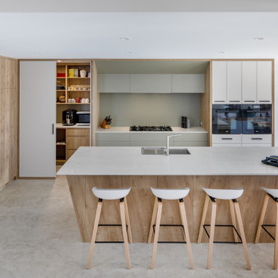 Kitchen - large contemporary l-shaped porcelain tile and gray floor kitchen idea in Perth with a double-bowl sink, quartz countertops, green backsplash, glass sheet backsplash, black appliances, an island, flat-panel cabinets, white cabinets and white countertops