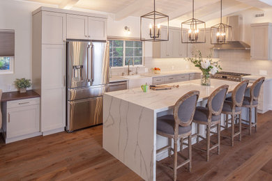 Example of a huge transitional l-shaped medium tone wood floor and brown floor open concept kitchen design in San Francisco with a farmhouse sink, shaker cabinets, white cabinets, marble countertops, white backsplash, subway tile backsplash, stainless steel appliances, an island and white countertops