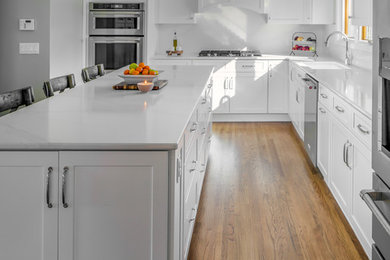 L-shaped brown floor eat-in kitchen photo in Other with shaker cabinets, white cabinets, quartz countertops, white backsplash, stainless steel appliances, an island and white countertops