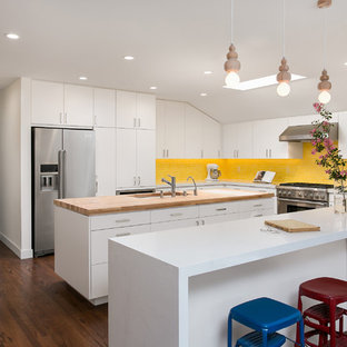 Photo of a mid-sized midcentury u-shaped eat-in kitchen in Los Angeles with a double-bowl sink, flat-panel cabinets, white cabinets, wood benchtops, yellow splashback, ceramic splashback, stainless steel appliances, medium hardwood floors, with island and brown floor.