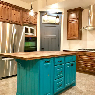 Idée de décoration pour une cuisine américaine style shabby chic en L de taille moyenne avec un placard avec porte à panneau surélevé, des portes de placard en bois brun, un plan de travail en bois, une crédence beige, un électroménager en acier inoxydable, un sol en carrelage de céramique et un îlot central.