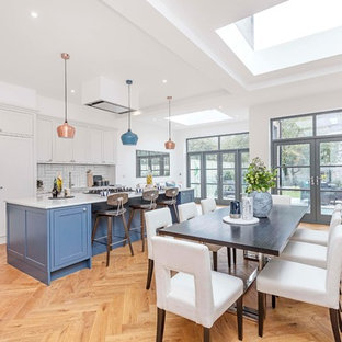 Inspiration for a classic galley kitchen/diner in London with a submerged sink, shaker cabinets, blue cabinets, white splashback, integrated appliances, medium hardwood flooring, an island, brown floors and white worktops.