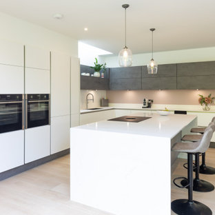 Photo of a large contemporary l-shaped kitchen/diner in Hampshire with a double-bowl sink, flat-panel cabinets, white cabinets, quartz worktops, white splashback, marble splashback, stainless steel appliances, porcelain flooring, an island, brown floors and white worktops.