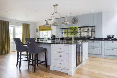 This is an example of an expansive farmhouse l-shaped open plan kitchen in Kent with an integrated sink, shaker cabinets, grey cabinets, granite worktops, metallic splashback, mirror splashback, stainless steel appliances, medium hardwood flooring, an island and brown floors.