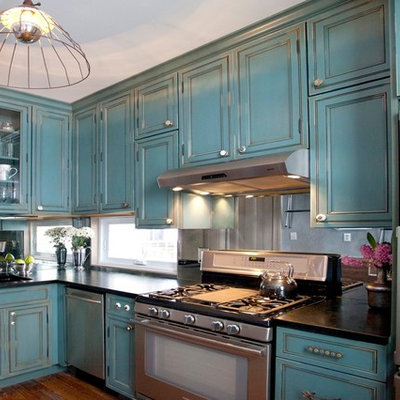 Elegant l-shaped enclosed kitchen photo in New York with stainless steel appliances, blue cabinets, soapstone countertops, mirror backsplash and beaded inset cabinets