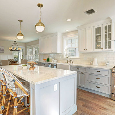 Example of a transitional medium tone wood floor eat-in kitchen design in Los Angeles with a farmhouse sink, shaker cabinets, gray cabinets, marble countertops, white backsplash, subway tile backsplash, stainless steel appliances and an island