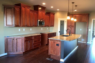 Example of a large classic u-shaped dark wood floor open concept kitchen design in Louisville with an undermount sink, raised-panel cabinets, brown cabinets, granite countertops and an island