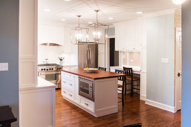 Eat-in kitchen - mid-sized traditional l-shaped medium tone wood floor and brown floor eat-in kitchen idea in Chicago with a double-bowl sink, recessed-panel cabinets, white cabinets, stainless steel appliances, an island, white backsplash and porcelain backsplash