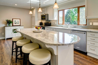 Example of a large classic single-wall medium tone wood floor and brown floor eat-in kitchen design in Columbus with an undermount sink, recessed-panel cabinets, beige cabinets, quartz countertops, green backsplash, subway tile backsplash, stainless steel appliances, an island and multicolored countertops