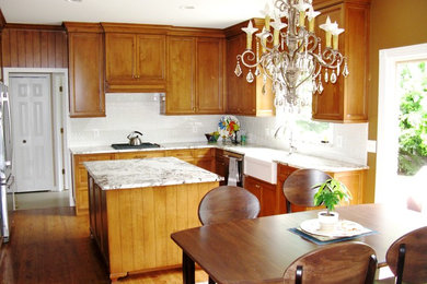 デトロイトにある高級な中くらいなトラディショナルスタイルのおしゃれなキッチン (エプロンフロントシンク、インセット扉のキャビネット、中間色木目調キャビネット、御影石カウンター、白いキッチンパネル、セラミックタイルのキッチンパネル、シルバーの調理設備、無垢フローリング、茶色い床) の写真