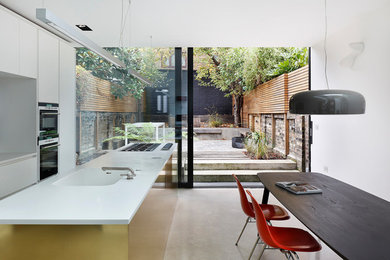 На фото: большая параллельная кухня в стиле модернизм с обеденным столом, накладной мойкой, плоскими фасадами, белыми фасадами, техникой из нержавеющей стали, бетонным полом, островом и серым полом
