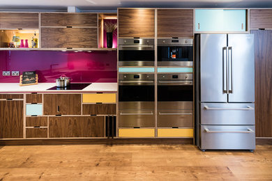 Inspiration for a retro kitchen in Other with flat-panel cabinets, medium wood cabinets, pink splashback, stainless steel appliances, medium hardwood flooring, no island and brown floors.