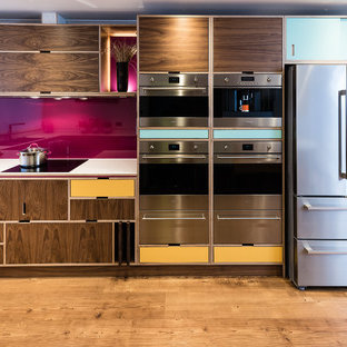 Inspiration for a retro kitchen in Other with flat-panel cabinets, medium wood cabinets, pink splashback, stainless steel appliances, medium hardwood flooring, no island and brown floors.
