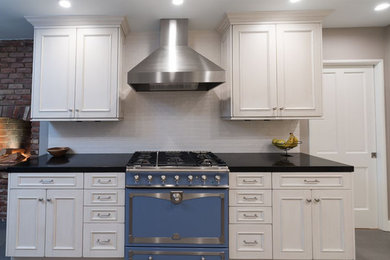 This is an example of a medium sized traditional galley enclosed kitchen in Los Angeles with a belfast sink, recessed-panel cabinets, white cabinets, engineered stone countertops, white splashback, metro tiled splashback, stainless steel appliances, porcelain flooring, a breakfast bar and grey floors.