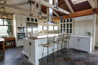 Photo of a large rural kitchen in San Francisco with a submerged sink, recessed-panel cabinets, white cabinets, engineered stone countertops, beige splashback, porcelain splashback, stainless steel appliances, slate flooring, an island, multi-coloured floors and white worktops.