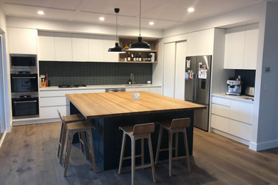 Mittelgroße Wohnküche in L-Form mit Arbeitsplatte aus Holz und Kücheninsel in Auckland