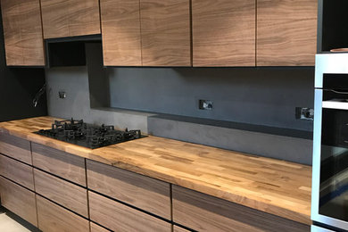 Design ideas for a medium sized modern single-wall open plan kitchen in London with a built-in sink, flat-panel cabinets, dark wood cabinets, wood worktops, grey splashback, stainless steel appliances, concrete flooring, an island and grey floors.