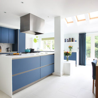 Ejemplo de cocina comedor moderna con armarios con paneles lisos, puertas de armario azules, salpicadero verde y electrodomésticos de acero inoxidable