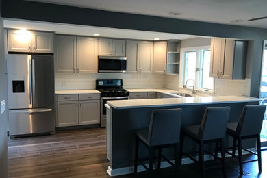 Eat-in kitchen - large transitional u-shaped brown floor eat-in kitchen idea in New York with an undermount sink, shaker cabinets, gray cabinets, quartz countertops, yellow backsplash, subway tile backsplash, stainless steel appliances, a peninsula and white countertops