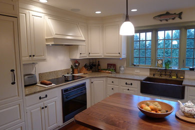 Inspiration for a mid-sized timeless l-shaped medium tone wood floor eat-in kitchen remodel in Boston with a farmhouse sink, white cabinets, quartz countertops, white backsplash, porcelain backsplash, paneled appliances, an island and raised-panel cabinets