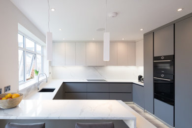 Photo of a large contemporary u-shaped open plan kitchen in Cheshire with a submerged sink, flat-panel cabinets, grey cabinets, marble worktops, white splashback, marble splashback, integrated appliances, vinyl flooring, a breakfast bar, brown floors and white worktops.