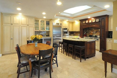 Photo of a medium sized traditional u-shaped kitchen/diner in Los Angeles with raised-panel cabinets, beige cabinets, granite worktops, multi-coloured splashback, stone tiled splashback, stainless steel appliances, ceramic flooring, an island and beige floors.