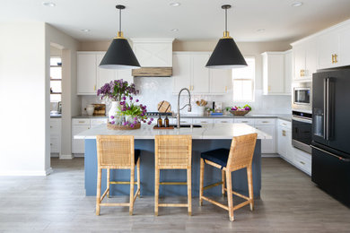 Mid-sized transitional l-shaped ceramic tile, gray floor and exposed beam eat-in kitchen photo in Orange County with a farmhouse sink, shaker cabinets, white cabinets, quartzite countertops, white backsplash, stone tile backsplash, black appliances, an island and white countertops