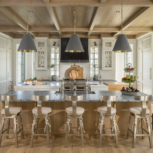 Immagine di una cucina tradizionale con lavello sottopiano, ante con riquadro incassato, ante bianche, paraspruzzi bianco, elettrodomestici in acciaio inossidabile, parquet chiaro e 2 o più isole