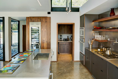 Ejemplo de cocina lineal moderna grande abierta con armarios con paneles lisos, puertas de armario grises, salpicadero verde, electrodomésticos de acero inoxidable, suelo de cemento y una isla