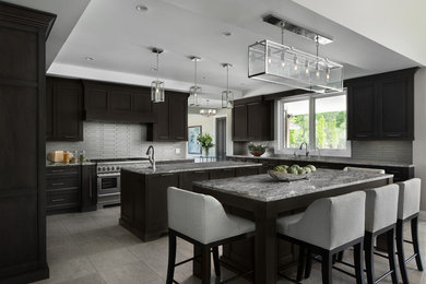 Inspiration for a transitional u-shaped gray floor kitchen remodel in Detroit with recessed-panel cabinets, dark wood cabinets, gray backsplash, matchstick tile backsplash, stainless steel appliances, two islands and gray countertops