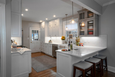 Inspiration for a mid-sized farmhouse l-shaped light wood floor eat-in kitchen remodel in Other with a farmhouse sink, shaker cabinets, white cabinets, quartz countertops, white backsplash, subway tile backsplash, stainless steel appliances, no island and white countertops