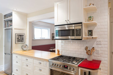 Small elegant galley medium tone wood floor enclosed kitchen photo in Ottawa with a farmhouse sink, recessed-panel cabinets, white cabinets, wood countertops, white backsplash, subway tile backsplash, stainless steel appliances and no island