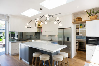 Inspiration for a coastal l-shaped medium tone wood floor and brown floor open concept kitchen remodel in Melbourne with an undermount sink, quartz countertops, metallic backsplash, stainless steel appliances, an island, flat-panel cabinets, white cabinets, mirror backsplash and gray countertops