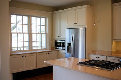 Foto de cocina de estilo de casa de campo de tamaño medio con armarios estilo shaker, puertas de armario blancas, salpicadero beige, electrodomésticos de acero inoxidable y una isla